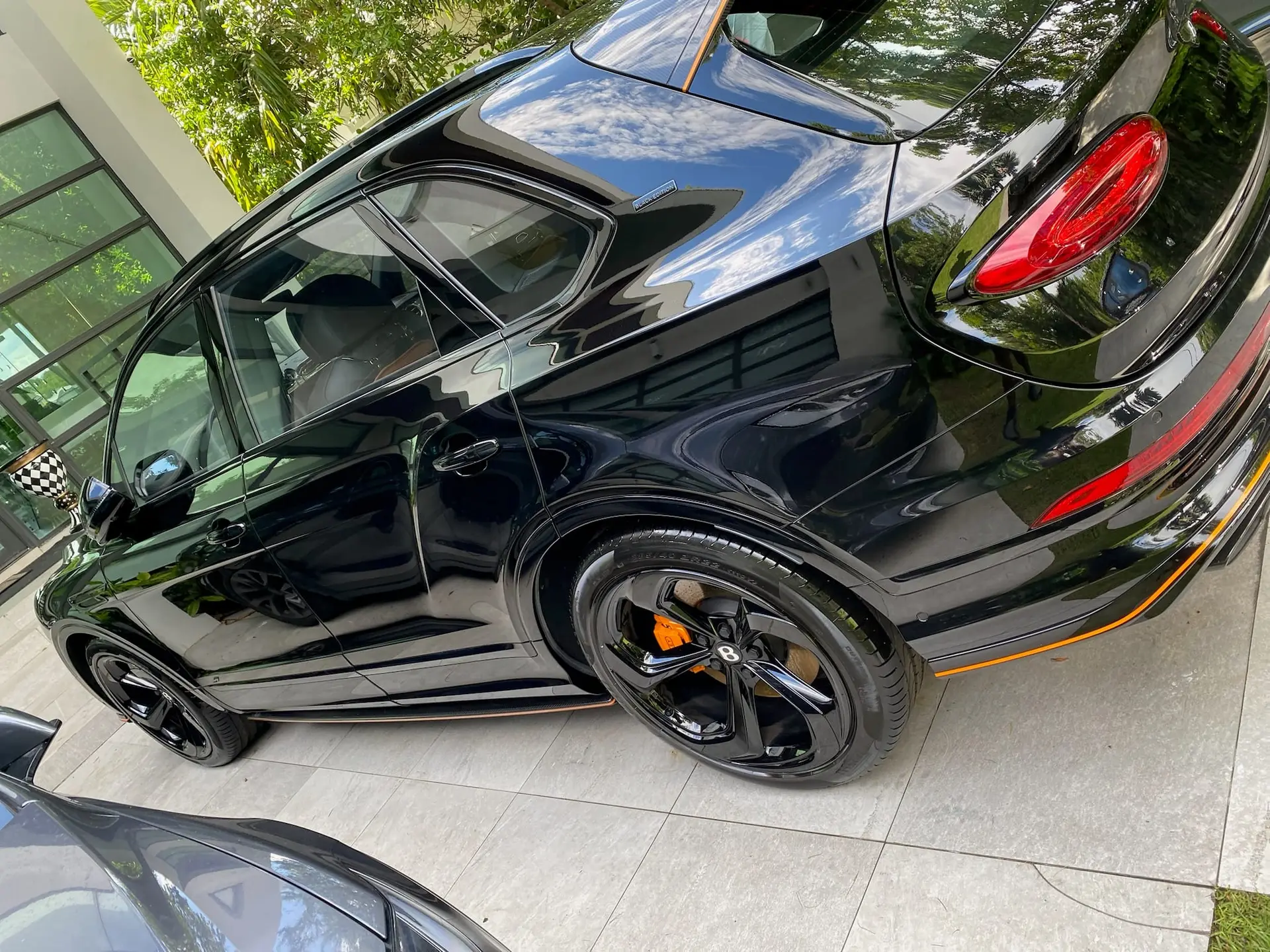 A black Bentley Bentayga finished to a mirror gloss, sky and palms reflected in the paint