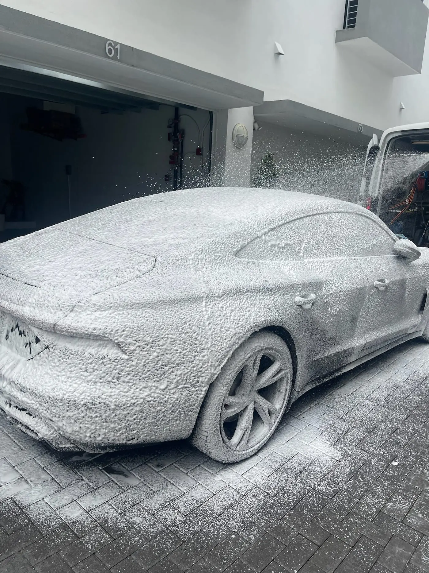 A car under a thick blanket of snow foam with the Scrub N Sudz van alongside